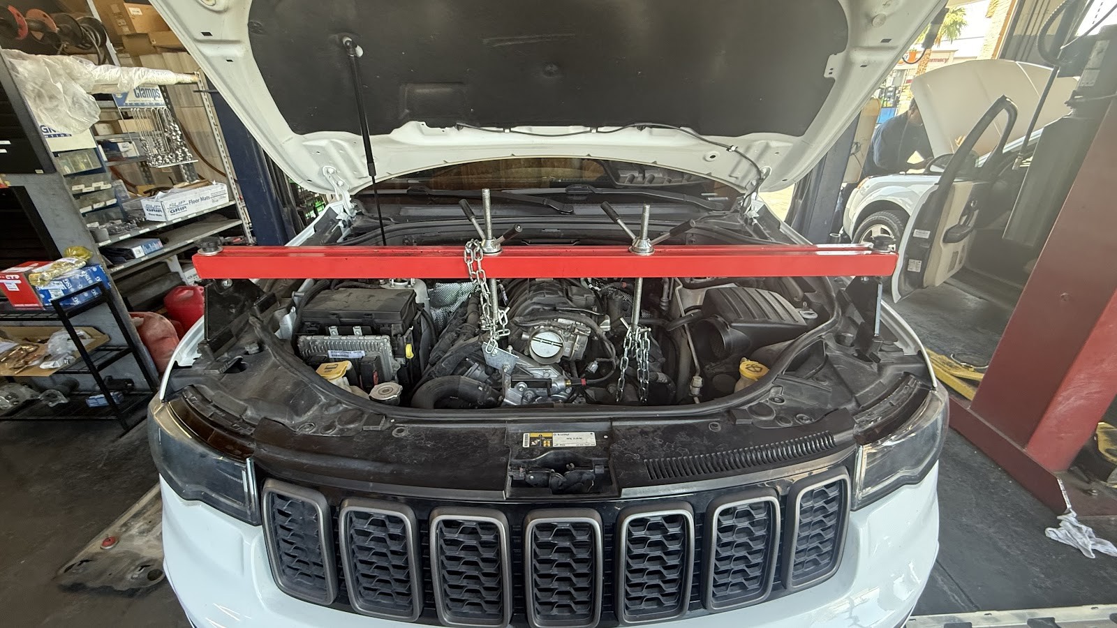 White Jeep Grand Cherokee with hood open and an engine support bar installed for engine service